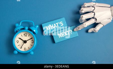 Roboterhand zeigt auf blaue Holzblöcke und sagt, was als Nächstes ist, neben einem blauen Wecker auf blauem Hintergrund, der die zukünftige Planung und KI repräsentiert. Stockfoto