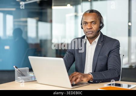 Männlicher, professioneller Kundendienstmitarbeiter, der ein Headset trägt und auf einem Laptop tippt und aktiv an der Kommunikation und Unterstützung in einer modernen Unternehmensumgebung beteiligt ist Stockfoto