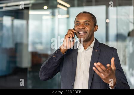 Erwachsener professioneller ethnischer Mann, der sich in der Telekommunikation engagiert, während eines Telefonanrufs selbstbewusst lächelt und Gesten gibt und Erfolg und professionelle Interaktion repräsentiert Stockfoto