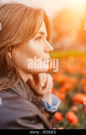 Frau Tulpe Sonnenuntergang lächelt nachdenklich in einem Feld von orangefarbenen Blumen während der goldenen Stunde Licht Flare Stockfoto