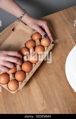 Pappeierkarton, gefüllt mit 12 braunen Hühnereiern auf einer hölzernen Küchenoberfläche, um eine tägliche Lebensmittelzubereitung oder Qualitätsprüfung zu erfassen Stockfoto