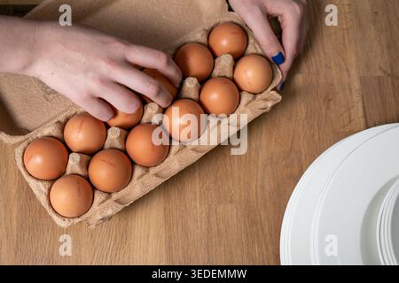 Pappeierkarton, gefüllt mit 12 braunen Hühnereiern auf einer hölzernen Küchenoberfläche, um eine tägliche Lebensmittelzubereitung oder Qualitätsprüfung zu erfassen Stockfoto