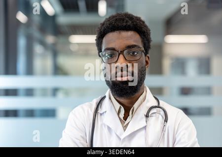 Selbstbewusstes afrikanisches Gesundheitspersonal, das in einer modernen klinischen Umgebung steht, einen weißen Labormantel und ein Stethoskop trägt und medizinisches Fachwissen und eine engagierte Patientenversorgung repräsentiert Stockfoto