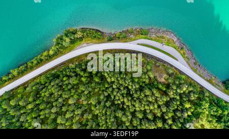 Dieses Drohnenfoto zeigt eine gewundene Küstenstraße, die sich durch dichten grünen Wald entlang des Randes eines türkisfarbenen Fjords in der Gegend von Stryn schlängelt Stockfoto