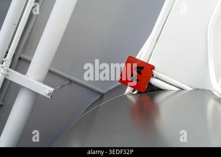Nahaufnahme eines roten Warnschilds auf einer metallischen Oberfläche, das industrielle Texturen und Reflexionen in einer städtischen Umgebung zeigt. Stockfoto