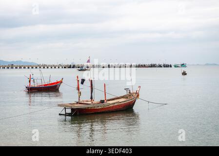 Eine ruhige Szene mit farbenfrohen Fischerbooten, die in ruhigen Gewässern in der Nähe eines Piers ankern. Der bewölkte Himmel und die ruhige Atmosphäre schaffen eine friedliche Küste Stockfoto