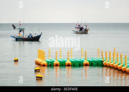 Zwei farbenfrohe Fischerboote ruhen auf ruhigem Wasser in der Nähe eines lebhaften Docks. Die Szene fängt eine ruhige Atmosphäre am Meer ein, perfekt für Strandliebhaber. Stockfoto