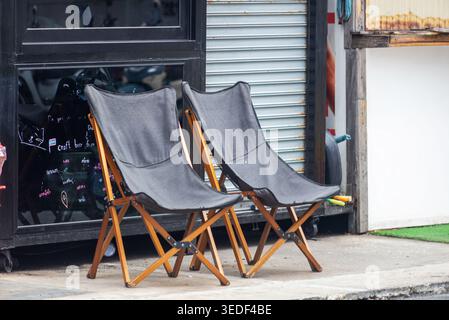 Zwei zusammenklappbare Stühle befinden sich in der Nähe einer Ladenfront und bieten eine Mischung aus minimalistischem Design und Komfort für Entspannung im Freien. Stockfoto