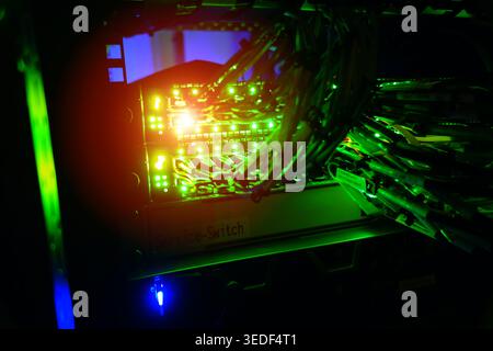 Eine faszinierende Ansicht eines Netzwerk-Switch-Panels, das von hellgrünen Lichtern beleuchtet wird und komplizierte Kabel und Technologien in einer Serverumgebung zeigt. Stockfoto