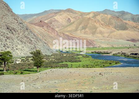 Ein sich windender blauer Fluss fließt durch ein üppiges grünes Tal in den trockenen Altai-Bergen der Westmongolei. Die Landschaft weist einen kontrastierenden grauen Geröll auf Stockfoto