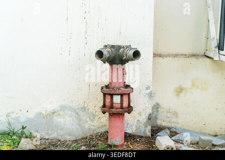Eine Nahaufnahme eines rostigen Hydranten, der an einer verwitterten Wand aufgestellt ist und die städtische Infrastruktur zeigt. Dieses Bild unterstreicht die Bedeutung des Brandschutzes Stockfoto