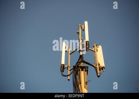 Ein hoher Mobilfunkturm mit Antennen steht deutlich vor einem klaren blauen Himmel und symbolisiert moderne Kommunikationstechnologie und Konnektivität in der Stadt Stockfoto