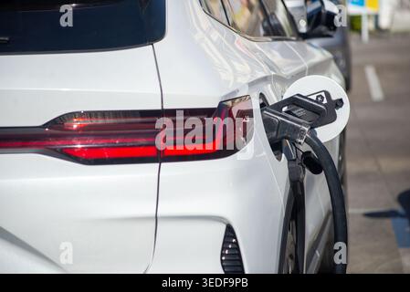 Nahaufnahme eines Elektrofahrzeugs, das an einer Station aufgeladen wird. Das Bild zeigt moderne Automobiltechnik und elektrische Energielösungen für Sust Stockfoto