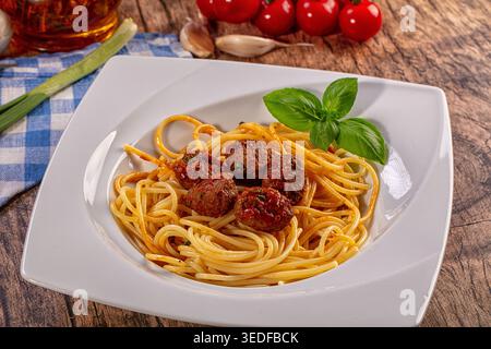 Herzhafte Spaghetti-Fleischbällchen-Platte. Goldene Pasta, reichhaltige Tomatensoße, herzhafte Fleischbällchen, frische Basilikumgarnitur. Rustikale Holztisch-Einrichtung mit Zutaten Stockfoto