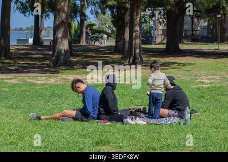 Eine Gruppe von Freunden und einem Kind, das ein Picknick genießt, und Paare auf dem Gras eines schattigen Parks an der Lagune in Chascomus, Argentinien. Lifestyle. Stockfoto