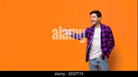 Junger Mann grüßt tagsüber mit einem Lächeln vor der Orange Wall Stockfoto