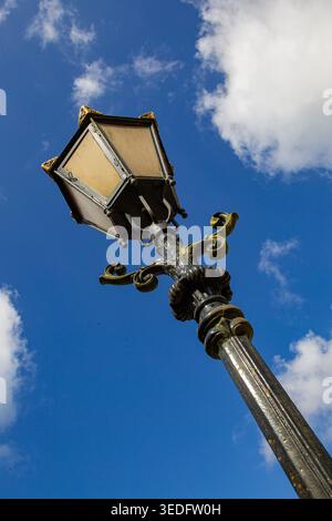 Blick auf eine verzierte Vintage-Straßenlaterne mit goldenen dekorativen Elementen vor einem hellblauen Himmel mit weißen Wolken auf Schloss Groeneveld in Baarn, Utrecht Stockfoto