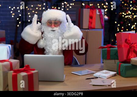 Schockierte den Weihnachtsmann mit Laptop und Geschenkboxen in der Post Stockfoto
