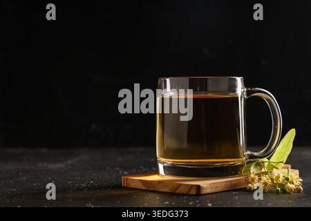 Glasbecher mit heißem Lindentee und Blumen auf schwarzem Hintergrund Stockfoto