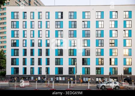 Berlin, Deutschland, 5. Mai 2026, symmetrische Vorderansicht einer modernen Wohnhausfassade mit hellen türkisfarbenen Akzentplatten und einer Bausitze Stockfoto