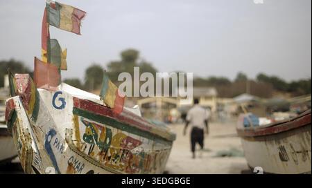 Bunte Fischerboote mit Fahnen, senegalesische Fahnen im Vordergrund, ein verschwommener Mann im Hintergrund, Cap Skirring, Casamance, Senegal Stockfoto