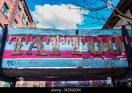 Nahaufnahme einer übergroßen bemalten Holzbank mit rustikalem „Tattoo“-Schild und Graffiti-Markierungen in Berlin-Alt-Treptow, Deutschland. Stockfoto