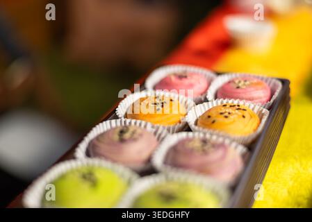 Nahaufnahme von verschiedenen süßen Gebäckbällchen in Pappbecher mit Sesam-Belag leuchtende Farben Dessertauswahl weiche Unschärfe Hintergrund Bäckerei Snack Konzept Stockfoto