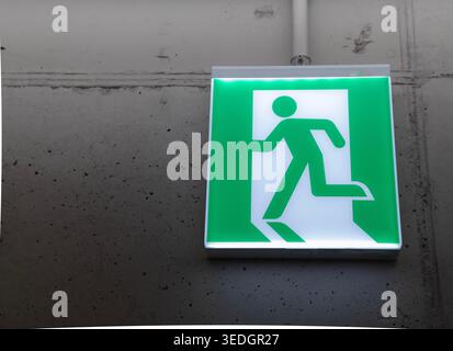 Notausgangstaste mit grünem Licht an Betonwand. Minimaler industrieller Innenraum mit Kopierraum, Sicherheits- und Evakuierungskonzept. Stockfoto