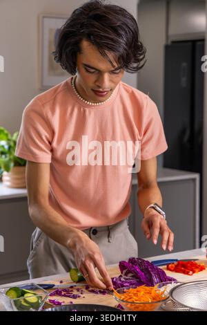 Mann in 20ern, der Purpurkohl mit Kochmesser auf Schneidebrett in der Küche hackt, Pfirsichhemd Stockfoto