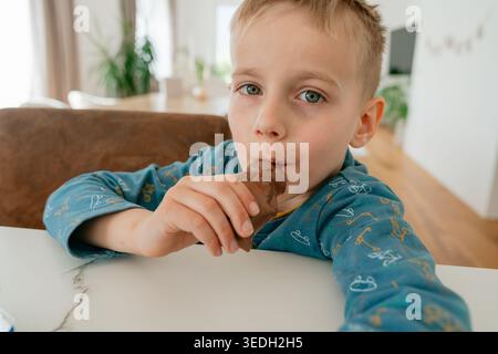 Junge isst Schokolade zu Hause. Kinder- und Lebensstil-Konzept. Kind genießt süßen Imbiss. Lässiger Heim-Moment. Stockfoto