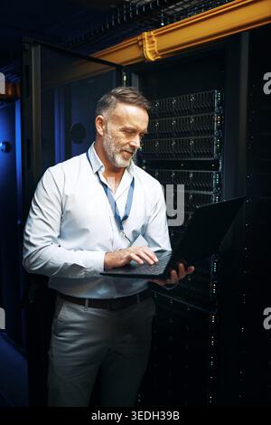 Ausgereifter Mann- und Serverraum mit Laptop für die Wartung der Cybersicherheit oder Netzwerksteuerung. Männlicher Mensch, IT-Techniker oder Ingenieur mit Computer oder Stockfoto
