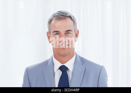 Mann mittleren Alters posiert für Firmenkopffoto im Studio in hellgrauem Anzug und marineblauer Krawatte. Executive, Porträt, professionell, formell, Jacke, Hemd Stockfoto
