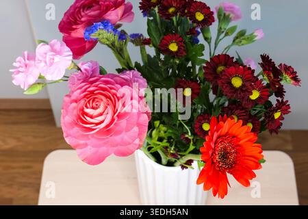 Blumenstrauß aus bunten Blumen in einer weißen Vase, die ein lebendiges botanisches Stillleben und eine dekorative Komposition schaffen. Stockfoto