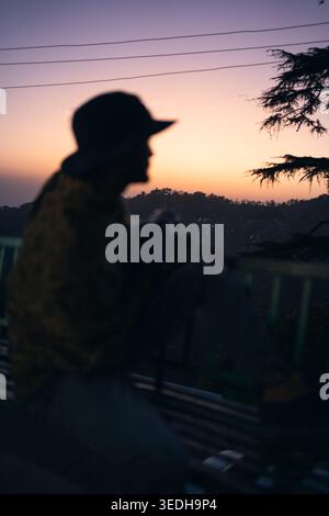 Eine Silhouette einer Person mit Hut, die einen Sonnenuntergang in Triund, Mcleodganj, Himachal Pradesh, Indien, ansieht. Stockfoto