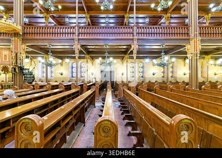 Die Menschen sitzen ruhig in der Dohany Street Synagoge in Budapest. Die hölzernen Bänke bilden Reihen in dem ruhigen Raum. Lichtfilterung durch Buntglas. Stockfoto