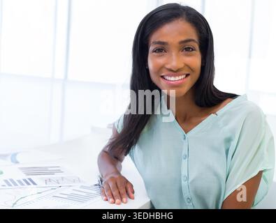 Afroamerikanerin, die Berichte und Diagramme auf weißem Bürotisch in mintwertiger Bluse, Kopierraum überprüft. Professionell, geschäftlich, Analytics, Daten, Dashboar Stockfoto