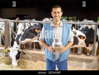 Ein Viehzüchter hält eine Milchjungfer mit einer Herde Kühe im Hintergrund in der Scheune Stockfoto