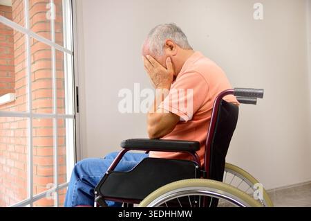 Trauriger älterer Mann, der auf Rollstuhl sitzt, im leeren Zimmer vor einem Fenster Stockfoto