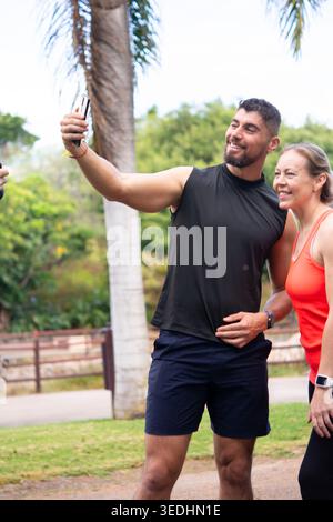 Sportlicher Mann und reife Frau lächeln während eines Selfie-Trainings im Freien in einem tropischen Park. Gesunder Lebensstil, Freundschaft, Technik Stockfoto
