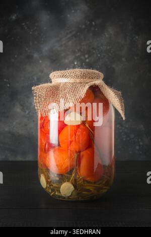 Gemüse-Tomate in Dosen in Glasgläsern auf dunklem Holzbrett. Leerzeichen für Text. Blick von oben. Verschiedene Arten von Dosen. Hausgemachte Erntevorbereitungen im Herbst. Hausaufgaben und Traditionen. Stockfoto