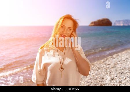 Frau Strandtelefon Glückliche Frau spricht auf Smartphone, während sie während der sonnigen Sommerferien am Kieselstrand steht Stockfoto