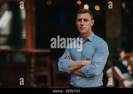 Selbstbewusster Geschäftsmann, der mit überkreuzten Armen in einem zwanglosen Meeting-Ambiente in einem Restaurant steht Stockfoto