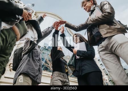 Studenten feiern mit einer Gruppe High Five draußen auf einem modernen Universitätscampus Stockfoto