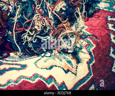 Orientalische Teppiche und Wollfäden auf dem Markt. Konzept „vom Material zum Produkt“. Selektiver Fokus auf die Gewinde. Getöntes Foto. Stockfoto
