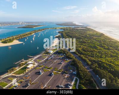 Ein atemberaubendes Luftbild zeigt einen Parkplatz, grünen Wald und Yachten, die bei Sonnenaufgang im ruhigen Wasser der Gold Coast vor Anker liegen. Stockfoto