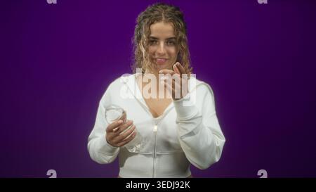 Frau, die eine Wasserflasche hält, die Hand an die Haare hält und mit dem Zeigefinger im Studio zeigt; Selbstvertrauen erfrischen. Stockfoto