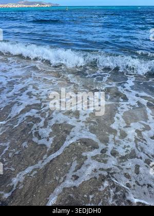 Weißer Meereswellen-Schaum, der über den dunkelgrauen vulkanischen Sand am Strand gewaschen wird. Stockfoto