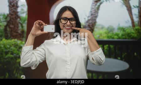 Frau, die eine Kreditkarte hält und vor dem Gebäude im Freien mit dem Finger auf die Karte zeigt; Vertrauensfinanzierung. Stockfoto