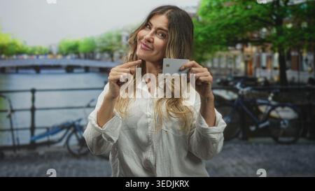 Frau, die eine Kreditkarte hält, zeigt auf der Straße an einer Kanalbrücke mit dem Finger auf die Karte; Selbstvertrauen stärkt ein Lächeln. Stockfoto