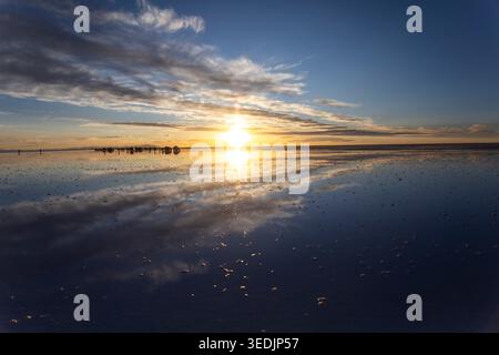 Ein spektakulärer Sonnenuntergang entfaltet sich über dem Salar de Uyuni, der weltweit größten Salzfläche im Departement Potosí in Bolivien, als dünne Schicht Wa Stockfoto